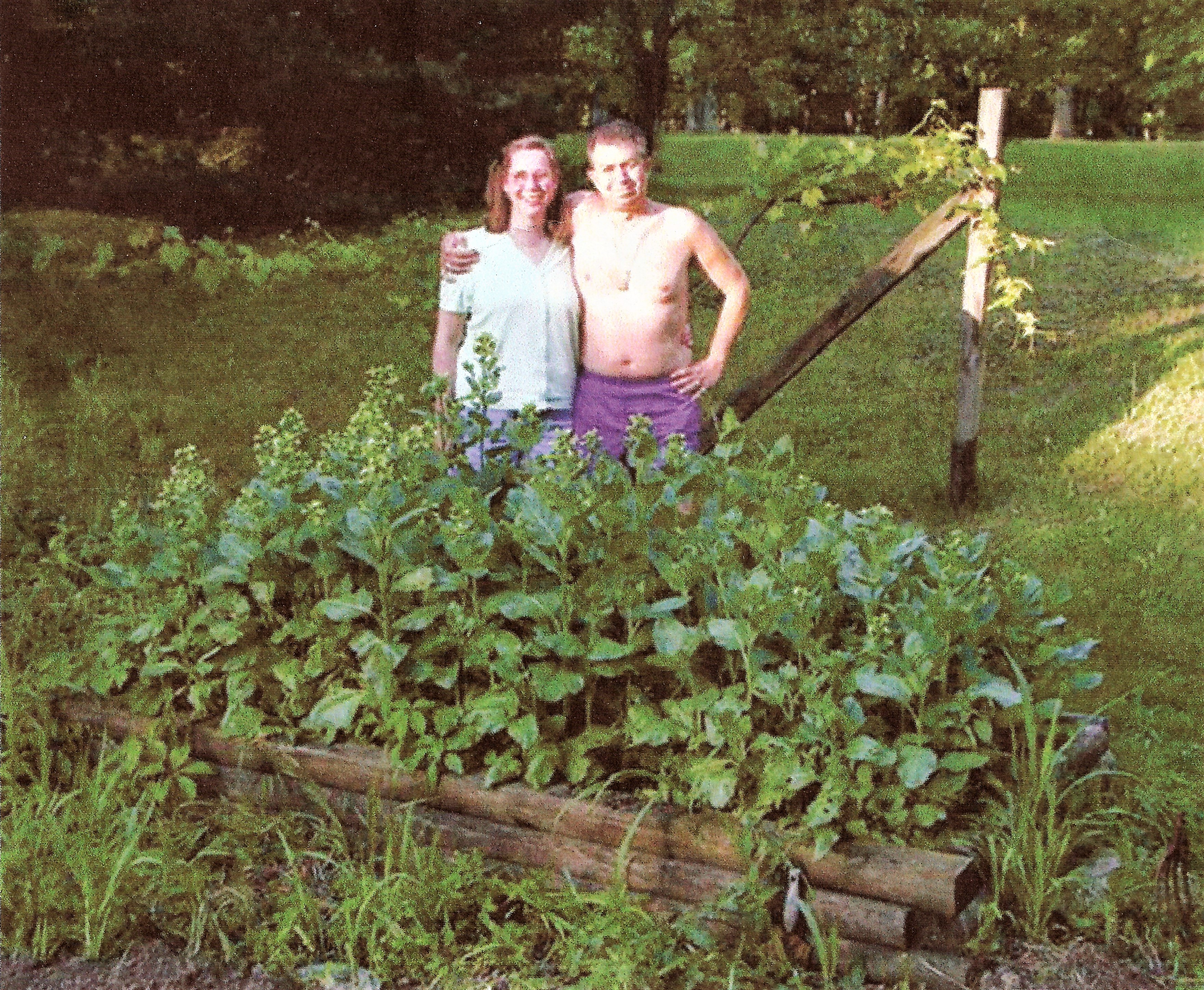 A husband and wife posed outdoors behind their tobacco garden.